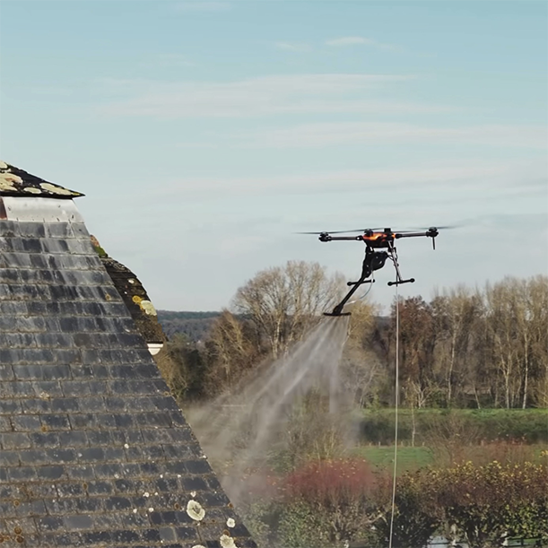 Drone pulvérisant un produit de démoussage sur une toiture en ardoise