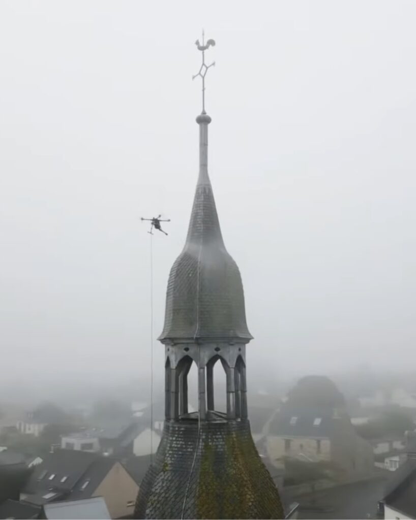 Drone réalisant le nettoyage d'un clocher d'église en hauteur par pulvérisation