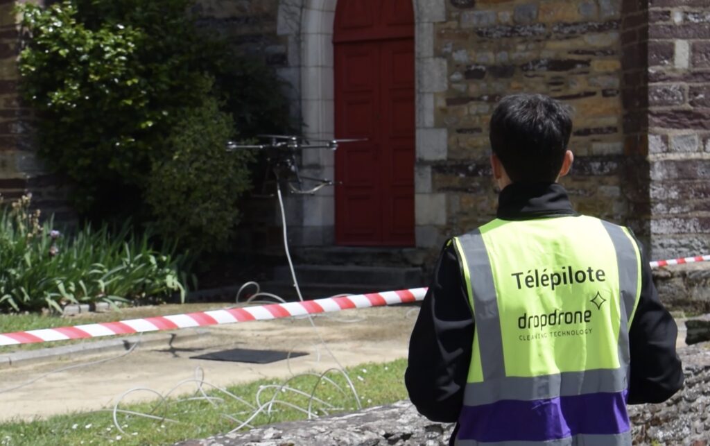 Télépilote Dropdrone contrôlant un drone de nettoyage devant un bâtiment